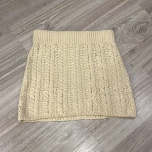 Beige stickad kjol från NA-KD - Säljer en mysig beige stickad kjol från NA-KD. Kjolen har ett ribbat mönster och är perfekt för kyligare dagar. Den är i storlek S och passar bra till en avslappnad stil.