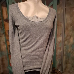 Grå tröja från esprit - Säljer en stilren grå tröja från esprit med rund halsringning och dekorativ spetsdetalj vid halsen. Tröjan har långa ärmar och en liten röd etikett vid nederkanten. Perfekt för en avslappnad look.