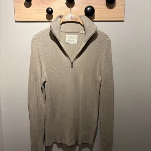 Beige stickad tröja med dragkedja - Snygg beige stickad tröja från jackandjones med dragkedja och hög krage. Perfekt för kyligare dagar med sin ribbade textur och långa ärmar. En stilren och tidlös design som passar till många tillfällen. Kolla profil för bundles