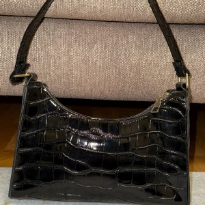 Svart axelväska i krokodilmönster - Svart axelväska med krokodilmönster och dragkedja. 