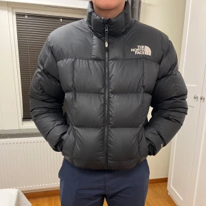 Svart pufferjacka från The North Face - Säljer en svart pufferjacka från The North Face. Jackan har en dragkedja framtill och är långärmad. Perfekt för kalla dagar med sin quiltade design som håller värmen. Den har en normal passform och är tillverkad i syntetmaterial.