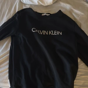 Svart tröja från Calvin Klein - Säljer en stilren svart tröja från Calvin Klein med vit logotyp på framsidan. Tröjan har långa ärmar och en klassisk passform. Perfekt för en avslappnad look.