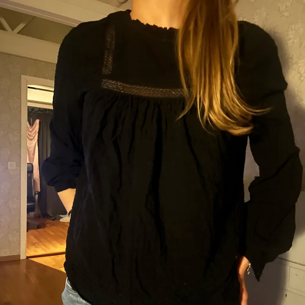 Elegant svart blus med spetsdetaljer vid halsen. Blusen har långa ärmar och en lös passform, perfekt för en stilren look.. Puserot.