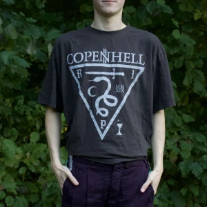 Svart Copenhell t-shirt - Säljer en svart t-shirt med tryck från Copenhell. Den har ett stort vitt tryck med text och symboler på framsidan. T-shirten är kortärmad och har en normal passform. Perfekt för festivaler eller vardagsbruk!
