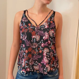 Blommig linne från Rails - Säljer ett superfint blommigt linne från Rails. Det har en mörk bas med vackra blommor i rosa, lila och orange. Linnet har smala axelband och en v-ringad design som ger en somrig känsla. Perfekt för varma dagar eller en kväll ute! 🌸