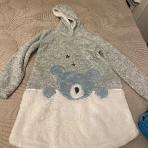 Sovkläder - Mjuka gosiga sovkläder för barn, i perfekt skick som använts få gånger. Mycket skön och varm. Har en luva och en tecknad björn som design. Passar både pojkar och flickor. Från Kappahl stl 134/140.