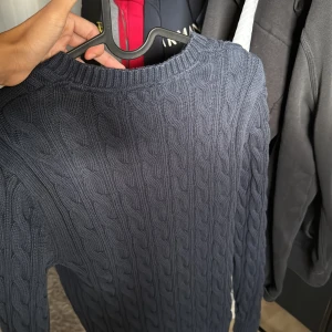 Mörkblå stickad tröja - Säljer en snygg blå stickad tröja. Den har ett klassiskt flätmönster och är perfekt för kyliga dagar. Tröjan är i storlek S och har långa ärmar. Perfekt för både höst och vinter!