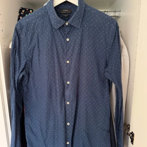 Blå prickig skjorta från Zara - Säljer en snygg blå skjorta från Zara i slim fit. Den har ett diskret prickigt mönster och knappar fram. Perfekt för både vardag och fest! 🕺