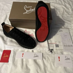 Christian Louboutin skor - Christian Louboutin sneakers i svart mocka med den ikoniska röda sulan och stilrena nitar. Helt oanvända, levereras i originalförpackning med äkthetskort och kvitto. 