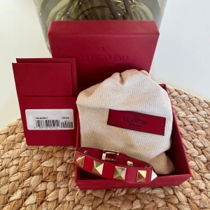 Valentino armband  - Rött valentino armband med guldiga nitar. Endast använt vid speciella tillfällen så fortfarande i väldigt fint skick. Originallådan med tillhörande lappar finns kvar. 