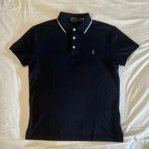 Mörkblå pikétröja från Ralph Lauren - Säljer en snygg mörkblå pikétröja från Ralph Lauren. Med stretchigt material (42% Polyester, 58% bomull). Varan är i mycket fint skick utan några skavanker, (9/10) om inte (10/10). Mått: Längd från axeln: 65 cm Midjemått: 48,5 cm. Perfekt för både vardag och lite finare tillställningar! Detta är en gammal modell och den går inte få tag på längre. Fundera inte om att kontakta vid ytterligare frågor! 😃👕