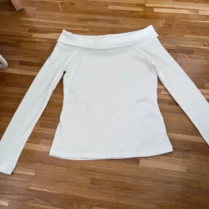 Vit ribbad offshoulder-tröja - Säljer en superfin vit ribbad tröja med offshoulder-design. Den är långärmad och perfekt för både vardag och fest. Tröjan har en tight passform som framhäver figuren. Perfekt för höst och vår!