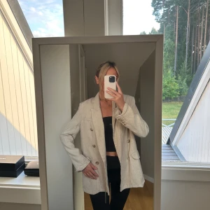 Beige kavaj - Säljer en snygg beige linnekavaj med dubbelknäppning. Den har en klassisk stil med långa ärmar och två fickor framtill. Perfekt för både vardag och fest!