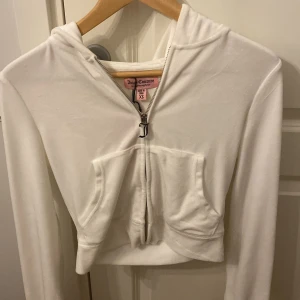 Vit hoodie från Juicy Couture - Säljer en superfin vit hoodie från Juicy Couture i storlek XS. Den har en dragkedja framtill och en snygg Juicy-logga i silver på ryggen. Perfekt för en chill dag eller när du vill känna dig extra glam. Helt ny aldrig använda! 🩶 