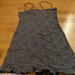 Klänning - Svart småblommig klänning i viskos med tunna axelband och liten volang i nederkant 