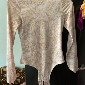 Beige mönstrad långärmad topp - Säljer en superfin beige topp med ett unikt mönster. Den har långa ärmar och en snygg passform som är perfekt för både vardag och fest. Materialet känns mjukt och skönt mot huden. Perfekt för höst och vår!