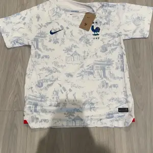 Säljer en snygg vit fotbollströja från Nike med blått mönster. Tröjan har korta ärmar och är i Dri-FIT-material, perfekt för träning eller match. KAN SÄNKAS VID SNABB AFFÄR! Cool Frankrike design vid brösten.