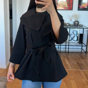 Svart kappa med knytband Calvin Klein 💞 - Säljer en superfin svart kappa med ett brett knytband i midjan. Den har en unik design med en stor krage och trekvartsärmar. Perfekt för höst och vår när du vill se stilren ut. Passar både till vardags och fest!💓