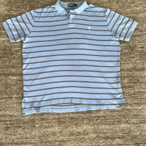 Ljusblå Ralph Lauren piké  - Fin vintage randig Ralph Lauren piké i ljusblå storlek Xl kan passa L om man vill ha loose fit den är i fint skick förutom ett pyttelitet hål vid kragen som man ser på bild.