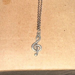 Silverfärgat halsband med G-klav - Säljer ett snyggt silverfärgat halsband med en hängande G-klav. Perfekt för musikälskare som vill ha en stilren accessoar. Kedjan är tunn och elegant, vilket gör den lätt att bära till både vardags och fest.