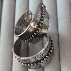Rustika silverörhängen med pärldetaljer - Säljer ett par unika och rustika örhängen i silver. De har en bred, halvcirkelformad design med en rad av små pärldetaljer längs mitten. Perfekta för att ge en bohemisk touch till din outfit!
