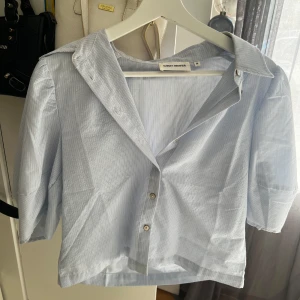 Randig skjorta från Ganni - Säljer en superfin randig skjorta. Den finns i både ljusblå och rosa färg. Skjortan har trekvartsärmar och knappar framtill. Perfekt för en avslappnad men stilren look!