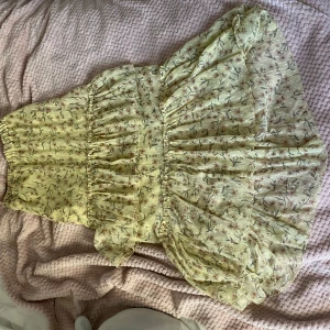 Blommig klänning från H&M - Säljer en superfin blommig och trendig långkjol från H&M i storlek XS. Den är ljusgul med ett sött blommönster och har volanger som ger en romantisk känsla. Perfekt för sommarens fester eller en mysig picknick i parken
