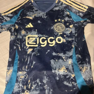 Ajax fotbollströja med mönster - En snygg Ajax fotbolls tröja, använd få tal gånger. Perfekt skick. Finns och mötas i Västerås 