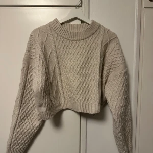Beige stickad tröja från H&M - Säljer en supermysig beige stickad tröja från H&M. Den har ett snyggt flätmönster på framsidan och ärmarna, vilket ger den en extra touch av stil. Tröjan är croppad och har långa ärmar, perfekt för höst och vinter. Den är i storlek XL och passar perfekt för en avslappnad och trendig look.