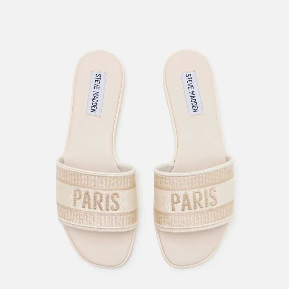 Säljer ett par snygga beige sandaler från Steve Madden i storlek 40. De har en bred rem med texten 'PARIS' och är perfekta för sommaren. Sandalerna är i materialet fabric och har en stilren design som passar till det mesta.. Skor.