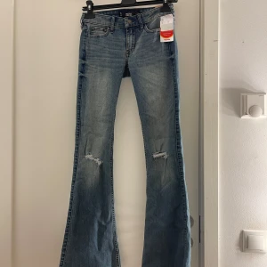 Blå jeans från Hollister - Säljer ett par snygga blå jeans från Hollister i nytt skick. De har en flare-stil och är lågmidjade med slitningar på knäna. Perfekta för både vardag och fest!🩷