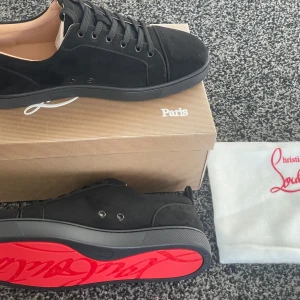 Svarta sneakers från Christian Louboutin - Säljer ett par snygga svarta sneakers från Christian Louboutin i mocka. De har den ikoniska röda sulan och klassisk snörning. Perfekta för att ge din outfit en lyxig touch. Skorna är i nytt skick och kommer med originalförpackning.