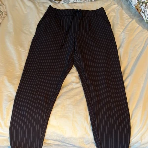 Mörkblå randiga byxor från ONLY - Säljer ett par mörkblåbyxor med vita ränder från ONLY. De har en bekväm elastisk midja med snörning för justerbar passform. Perfekta för både vardag och festliga tillfällen. Passar bra till en avslappnad stil eller uppklädd look. I nyskick och från ett djur och rökfritt hem!