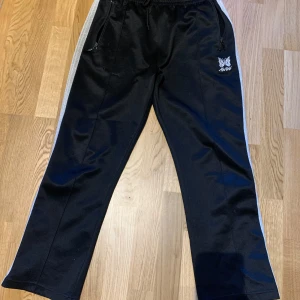 Needles x Awge Trackpants  - Svarta Needles x Awge Trackpants i storlek S, men passar även XS. Det finns ett litet hål, som dock knappt är synligt! (Se bild) Tveka inte på att skriva om ni har några frågor!