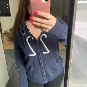 Säljer denna mörkblåa zip up hoodien med luva, fickor och med ett tryck på framsidan från Hollister i storlek M men tycker den är liten för att vara en M så skulle säga att den är mer som en S, använd fåtal gånger 