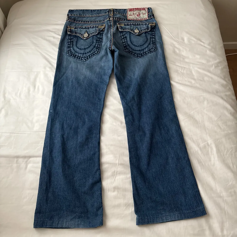 Säljer ett par skitcoola blå jeans från True Religion. Köpta på tradera och har inga tecken på användning! De har en bootcut-stil och är dekorerade med coola sömmar och knappar på bakfickorna. I modellen Billy Super T. Midjemått 47cm, längd:104cm. Jeans & Byxor.