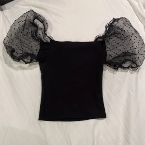 Svart topp med puffiga ärmar - Snygg svart topp med stora puffiga ärmar i transparent tyg med prickigt mönster. Passar pefekt till nyår eller på en utekväll