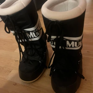Svarta Moon Boots med snörning - Snygga och varma svarta Moon Boots med vit vaddering och snörning. Perfekta för kalla vinterdagar med sin robusta design och höga skaft. Knappt använda 