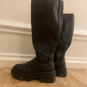 Svarta höga stövlar - Snygga svarta höga stövlar med grov sula. Perfekta för en stilren look under kyligare dagar. Tillverkade i ett robust material för extra hållbarhet.