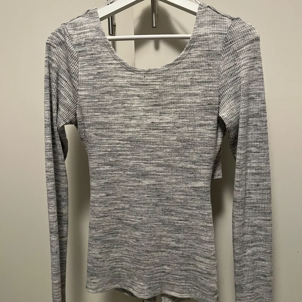 Snygg grå ribbad omlottopp med lång ärm. Perfekt för lager-på-lager-stil eller som statement-plagg. Den har en unik omlottdesign framtill som ger en modern touch.. Neuletakit & Villapaidat.