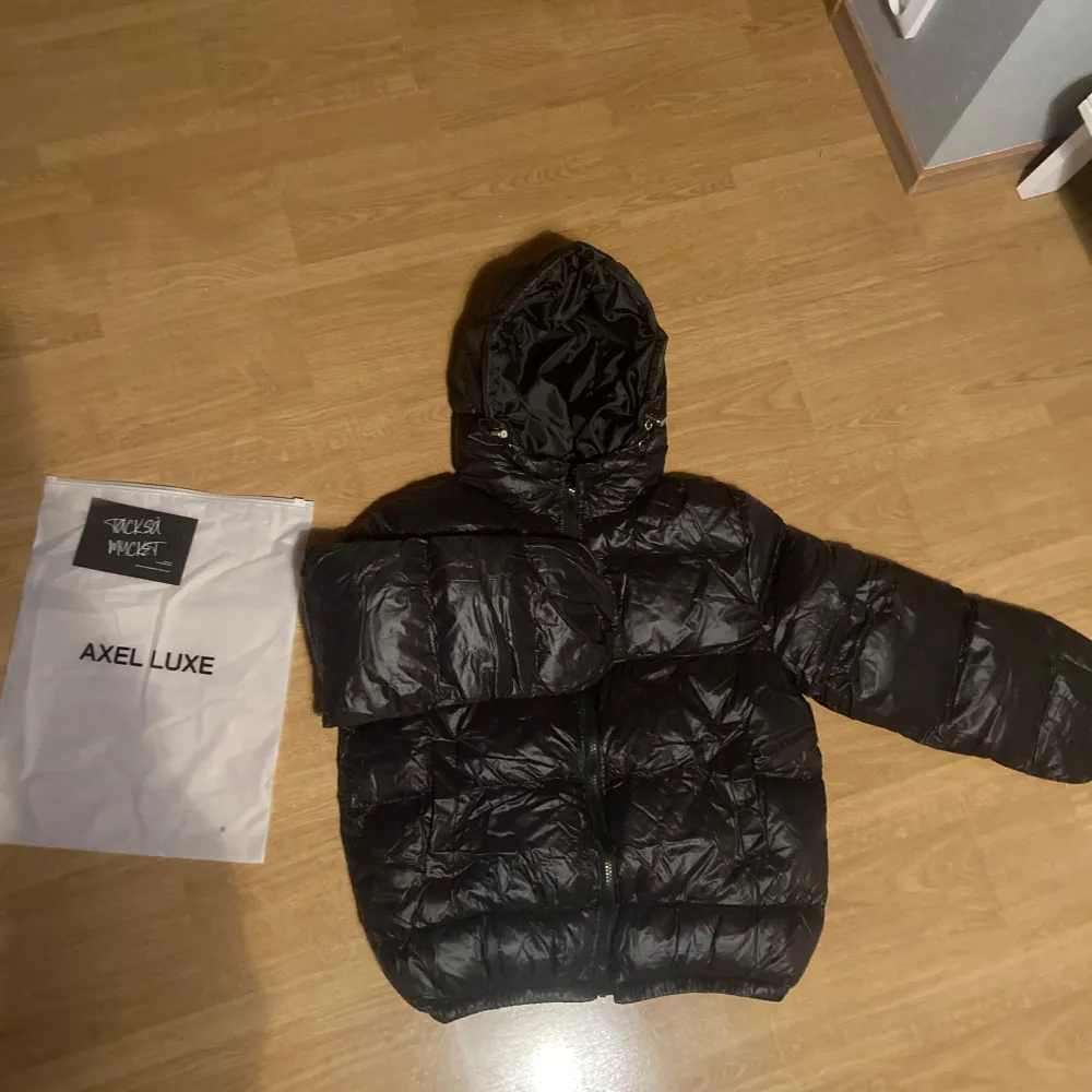 Snygg svart pufferjacka från Axel Luxe med huva och dragkedja. Perfekt för kyliga dagar med sin vadderade design som håller dig varm. Jackan har en glansig finish och är idealisk för både stil och komfort. Köpte den för nån vecka sen och den passade inte mig tyvärr så jag säljer den lite minde än vad ja köpte den för . Takit.