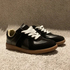 Gats - Snygga svarta sneakers med vita snören och brun sula. Skorna har en stilren design med detaljer i mocka och syntetmaterial. Perfekta för en avslappnad stil. Skorna har inget speciellt märke men är inspirerade av maison margiela. Dm för minsta fundering 😀.