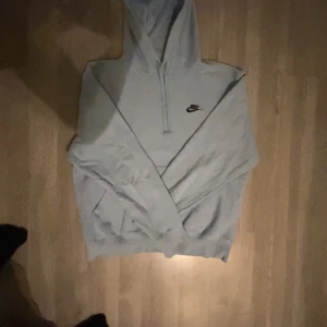 Ljus blå hoodie från Nike - Säljer en stilren grå hoodie från Nike med klassisk logga på bröstet. Perfekt för en avslappnad look med justerbar huva och ribbade muddar. Passar både till vardags och träning.