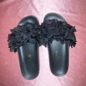 Svarta sandaler med blommig detalj - Snygga svarta sandaler med en unik blommig detalj på ovansidan. Perfekta för att ge en stilfull touch till din sommaroutfit.