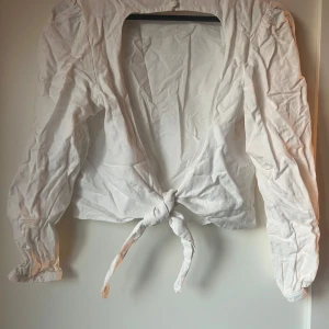 Vit blus med knyt baktill  - Säljer en stilren vit blus med knyt baktill. Blusen har långa ärmar och en rund halsringning. Perfekt för en chic och avslappnad look.