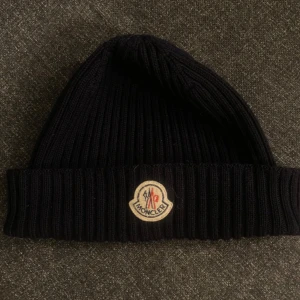 Svart ribbad mössa från Moncler - Säljer en Moncler mössa! Den köptes på NK i Göteborg men kommer tyvärr inte till användning längre. Äkthetsbevis på bild 2 där jag skannar QR-koden i mössan då kommer man direkt till moncler ma sida. 👍