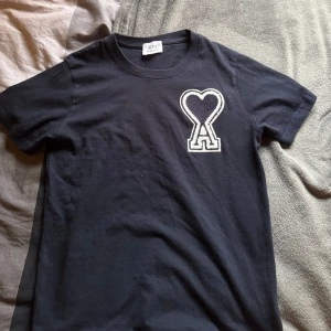 Mörkblå t-shirt från Ami Alexandre Mattiussi - Säljer min Snygga mörkblå t-shirt från Ami Alexandre Mattiussi med ett stort hjärta och bokstaven A broderat på bröstet. Perfekt för vilket sammanhang som helst. Pris går att diskutera 