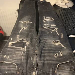 Svarta jeans från Dsquared2 - Säljer ett par svarta jeans från Dsquared2 med slitna detaljer och hål för en edgy look. Jeansen har en klassisk femficksdesign och knappgylf. Perfekta för dig som vill ha en unik stil.