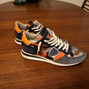 Philippe Model Camouflage - Snygga sneakers från Philippe Model med ett unikt camouflage-mönster i orange, blått och beige. Skorna är perfekt nu till vintern och sitter väldigt bekvämt, priset är inte hugget i sten så hör av er!