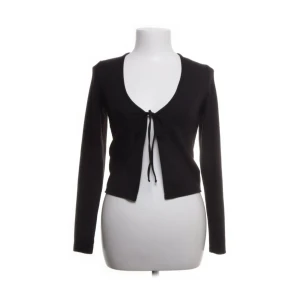 Svart ribbad kofta - Snygg svart ribbad kofta med knyt framtill. Den har en djup v-ringning och långa ärmar, perfekt för lager-på-lager-stil. En stilren och mångsidig topp för alla tillfällen.